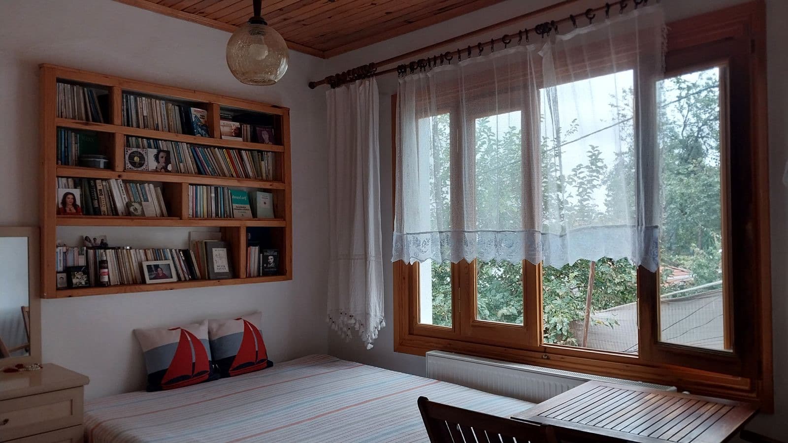 A bright bedroom with bookshelves and sheer curtains