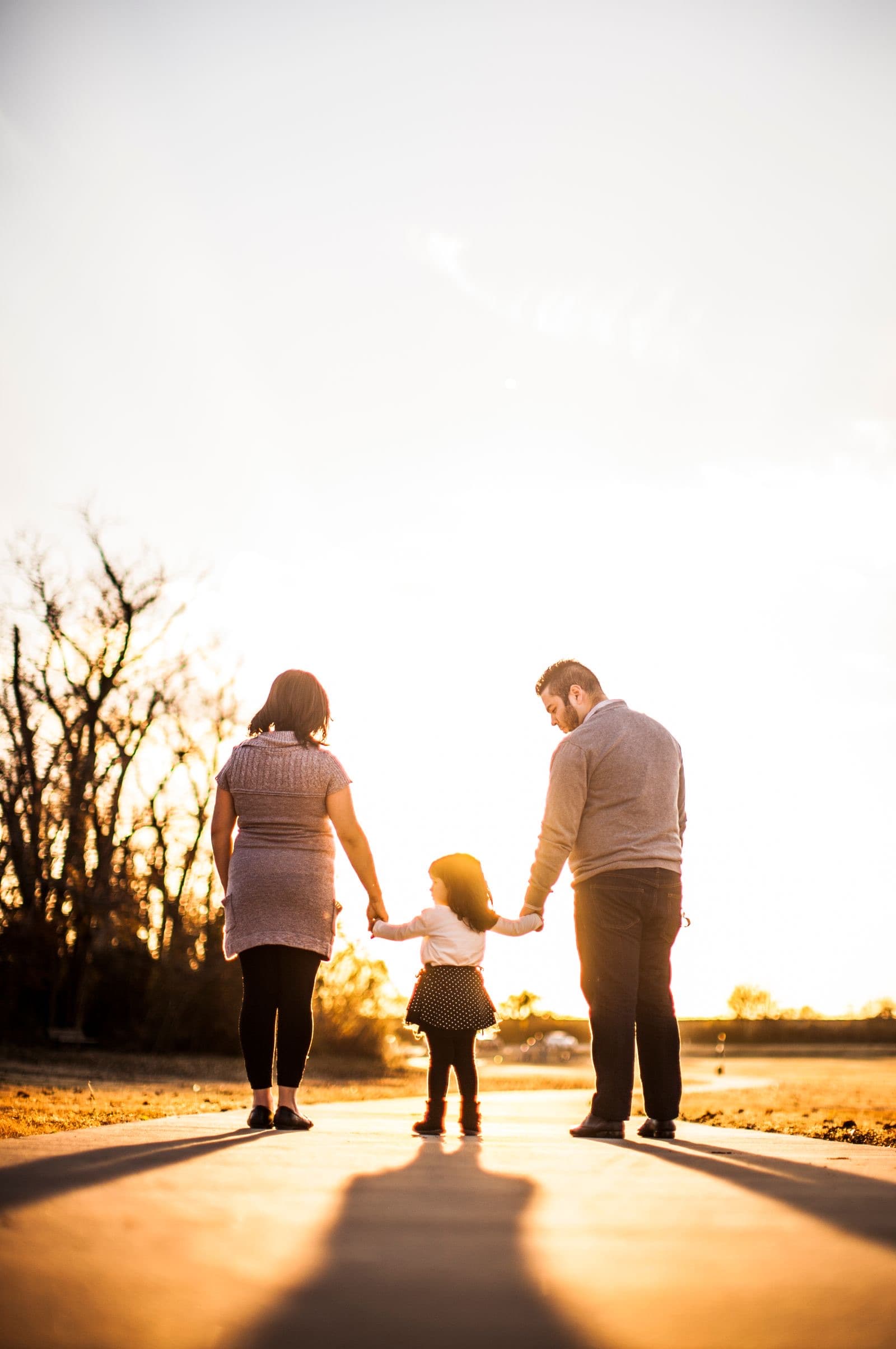 A family of three walking hand in hand at sunset