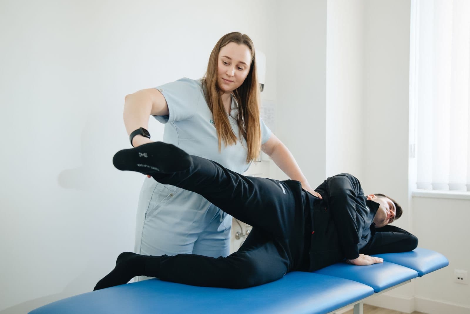 A physiotherapist guiding a patient through a hip stretch on a treatment table